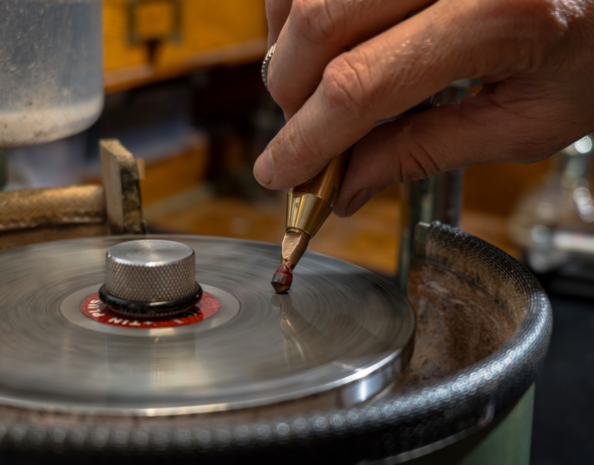 Stonecutter faceting red garnet stone on the metal dop stick into the round stone shape